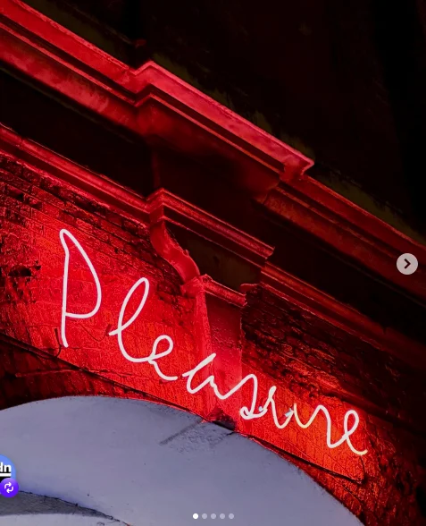 Cartel de neón Pleasure sobre un arco de ladrillo